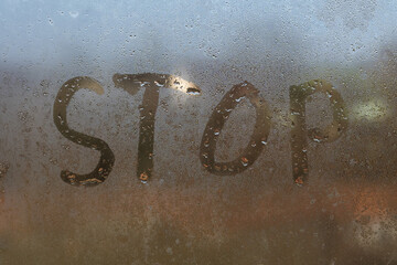 the word stop written on night wet window glass close-up with blurred background