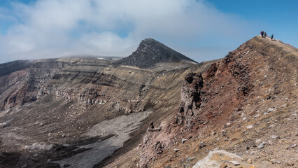 The crater of an active volcano. Close-up. The layered structure of the slopes is visible. On the edge of the ridge, against the blue sky - tiny silhouettes of people. Kamchatka. Gorely Volcano