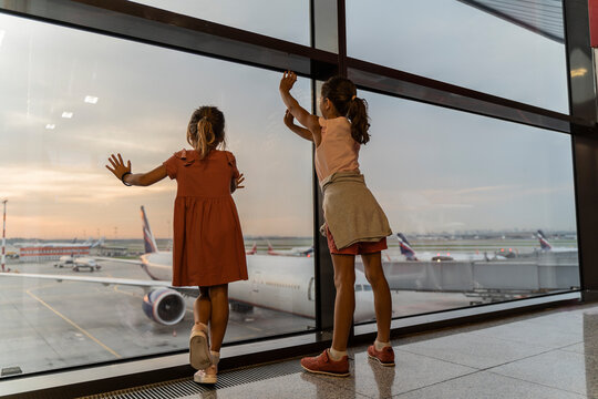 Little sister girls together at the airport waiting for boarding near the big window. Adorable children looks at the planes at the airport. Waiting to leave for a family summer vacation