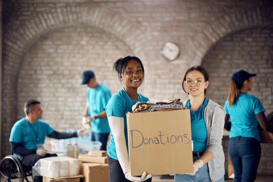 Happy female volunteers with donation dox at humanitarian aid center looking at camera.