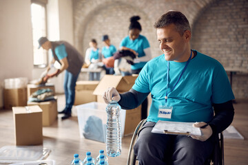 Happy volunteer in wheelchair organizing bottled water at donation center.