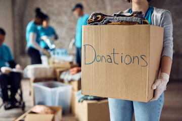 Close up of woman holds cardboard box filled with donated clothes while volunteering at charity...