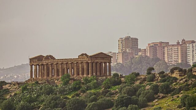 Panorama shot of historic Valle dei Templi archaeological site with city in background during misty and sunny day in Sicily,Italy