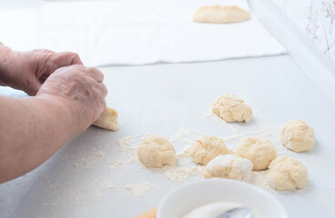Senior woman hands making pies with apple filling on a white kitchen table with wooden rolling pin on background. Selective focus. Cooking at home concept. Tradition home-made food