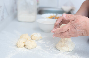 Senior woman hands form blanks for pies on a white kitchen table with blurred grated apple and sugar on background. Selective focus. Process of making pies with apple filling. Cooking at home concept