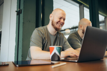 Fototapeta premium Unshaven happy man using laptop while sitting in cafe
