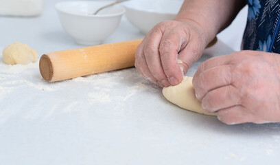Senior woman hands making pies with apple filling on a white kitchen table with wooden rolling pin on background. Selective focus. Cooking at home concept. Tradition home-made food