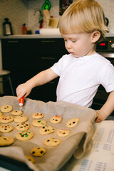 A little blond boy of two years old is cooking homemade cookies in the kitchen