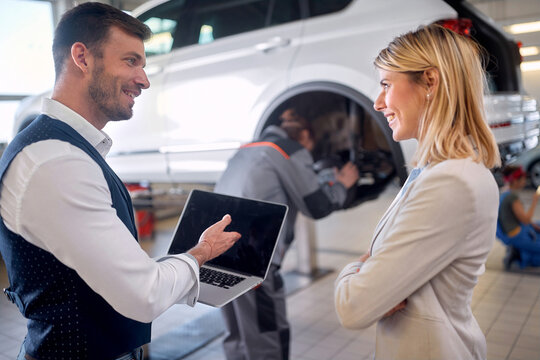 Man and woman in auto service showing laptop
