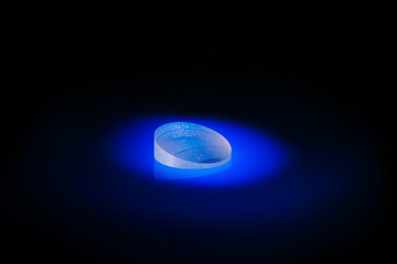 A glass transparent round object lying on a black surface, painted blue. Prism