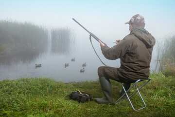 Man hunter charges the shotgun near rive bank at sunrise.  Duck Hunting.