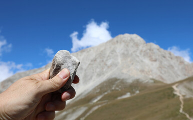 hand of the geologist holding a stone and the mountain called Gran Sasso in the background in the Abruzzo in central Italy