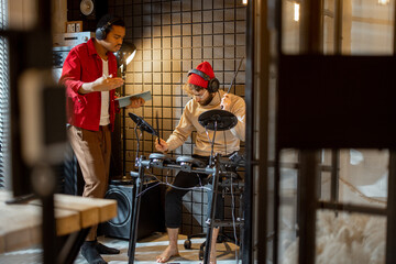 Two stylish men playing electric drums, composing electronic music at small recording studio. Small...