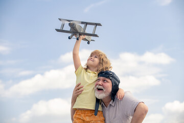 Grandfather and son enjoying play with plane together on blue sky. Cute child with granddad playing outdoor. Generations ages.