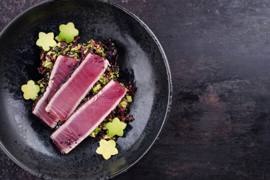 Modern style traditional Japanese gourmet seared tuna fish steak tataki with Sakura avocado, and mixed red brown rice served as top view in a Nordic design bowl with copy space right