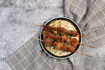 Kebabs on skewers with herbs on a flatbread on a round plate on a dark gray background. Top view, flat lay