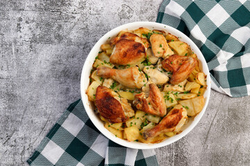 Homemade Roasted Chicken with Potatoes, onions and herbs  in a white baking dish on a dark grey background. Top view, flat lay