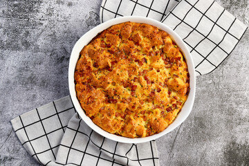 Breakfast Strata casserole with ham, herbs, cheese and cream in a white baking dish on a dark grey background. Top view, flat lay. - obrazy, fototapety, plakaty