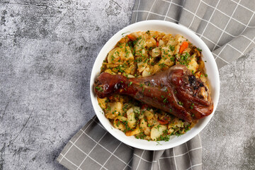 Oven baked Turkey drumstick with potatoes and vegetables in a white baking dish on a dark grey background. Top view, flat lay