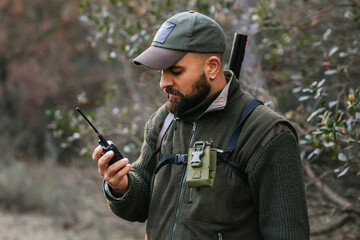 Bearded male hunter using walkie talkie in forest
