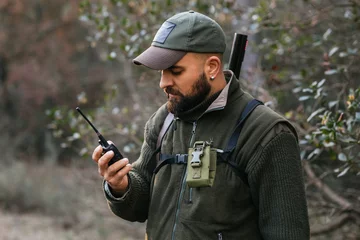 Foto op Canvas Bearded male hunter using walkie talkie in forest © Jordi Mora