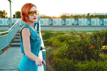 Beautiful young woman with short ginger hair walks around city against backdrop of sunset. Girl in sunglass. Spring mood.