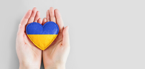 Pray for Ukraine banner. Female hands hold a heart with the flag of ukraine isolated on a blue background. Ukraine's Independence Day.