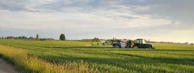 Modern tractor with irrigation system working on a green plowed agricultural field at sunset. Summer rural scene. Environment, special equipment, technology, farm industry © Alex Stemmer