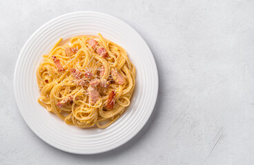 A portion of pasta carbonara with bacon, parmesan cheese and egg on a light gray background.