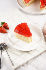 a Piece of a three-layered cake with vanilla pudding, strawberry jelly and fresh strawberries on a white marble background