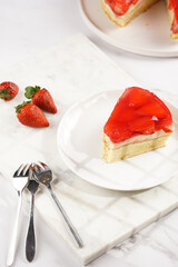 a Piece of a three-layered cake with vanilla pudding, strawberry jelly and fresh strawberries on a white marble background