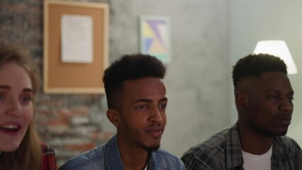 Young black guys students and blonde woman jump to celebrate college team victory in hostel lounge slow motion. Emotional sports fans enjoy great match