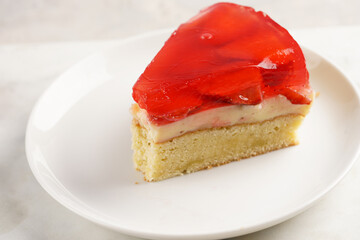 a Piece of a three-layered cake with vanilla pudding, strawberry jelly and fresh strawberries on a white marble background