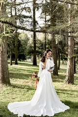 Fototapeta premium The groom hugs a beautiful bride in a white long wedding dress in the forest