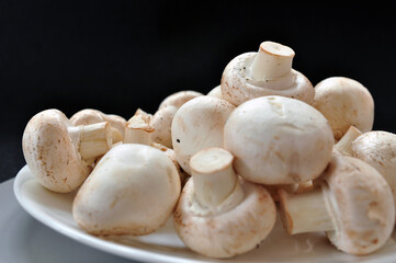 Nice fresh white mushrooms on the plate close up on black background