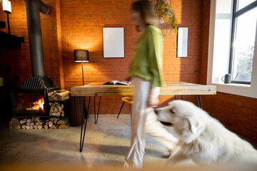 Living room interior in loft style with wooden table and burning fireplace at home. Motion blurred person passing by with her dog