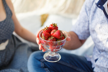 person holding translucent glass cup of strawberries in hand