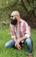 Naklejka na ściany i meble image of a bald man with beard using sunglasses posing on a green area