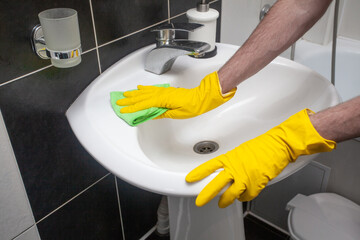 Hands in protective gloves cleaning sink and faucet using microfiber cloth and detergent, concept...
