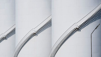 Sunlight on surface of spiral staircases on 3 white storage fuel tanks in oil industrial area