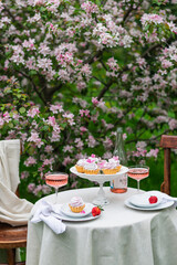 Table set on a white tablecloth on a sunny day, cherry blossom, cupcake, wine. Outdoor, picnic, brunch, spring mood. Soft focus