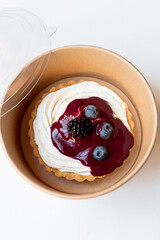 Cheesecake tart with berry jam and blueberries on paper food container. Delivery concept.