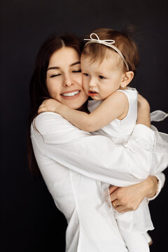 Close up of brunette young mother laying and holding baby girl. Attractive woman smiling and hugging her little daughter on the white background, posing in studio, photoshoot concept.