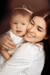Lovely mother hold in arms little daughter. Young brunette slim attractive woman and small child girl in fashionable dress smiling and laughing together