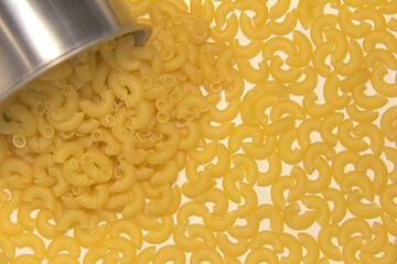 Yellow pasta is poured from a metal mug. Top view.