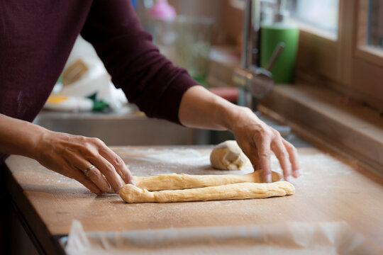 female hands roll and shape dough to bake an easter braid