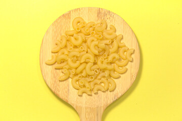 Yellow raw pasta on a kitchen spatula. On a yellow background. Top view. Close up.