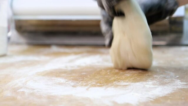 Professional cook kneads the dough and puts it into special rolling machine, close-up 4k footage