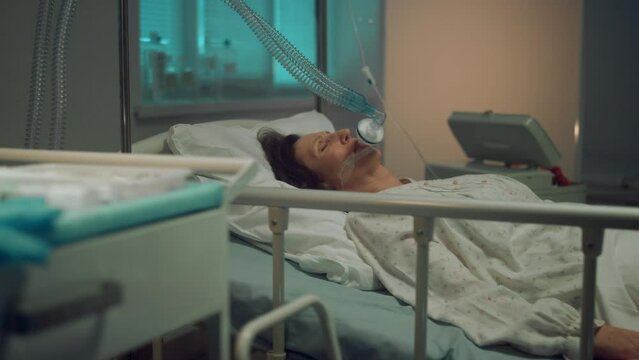 Sick woman oxygen mask lying in hospital bed. Terminally ill person in clinic.