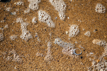 Engagement ring on a beach sand beside a sea wave